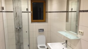 Moderni kylpyhuone, jossa on lasinen suihkuseinä, wc ja peilillä varustettu pesuallas.