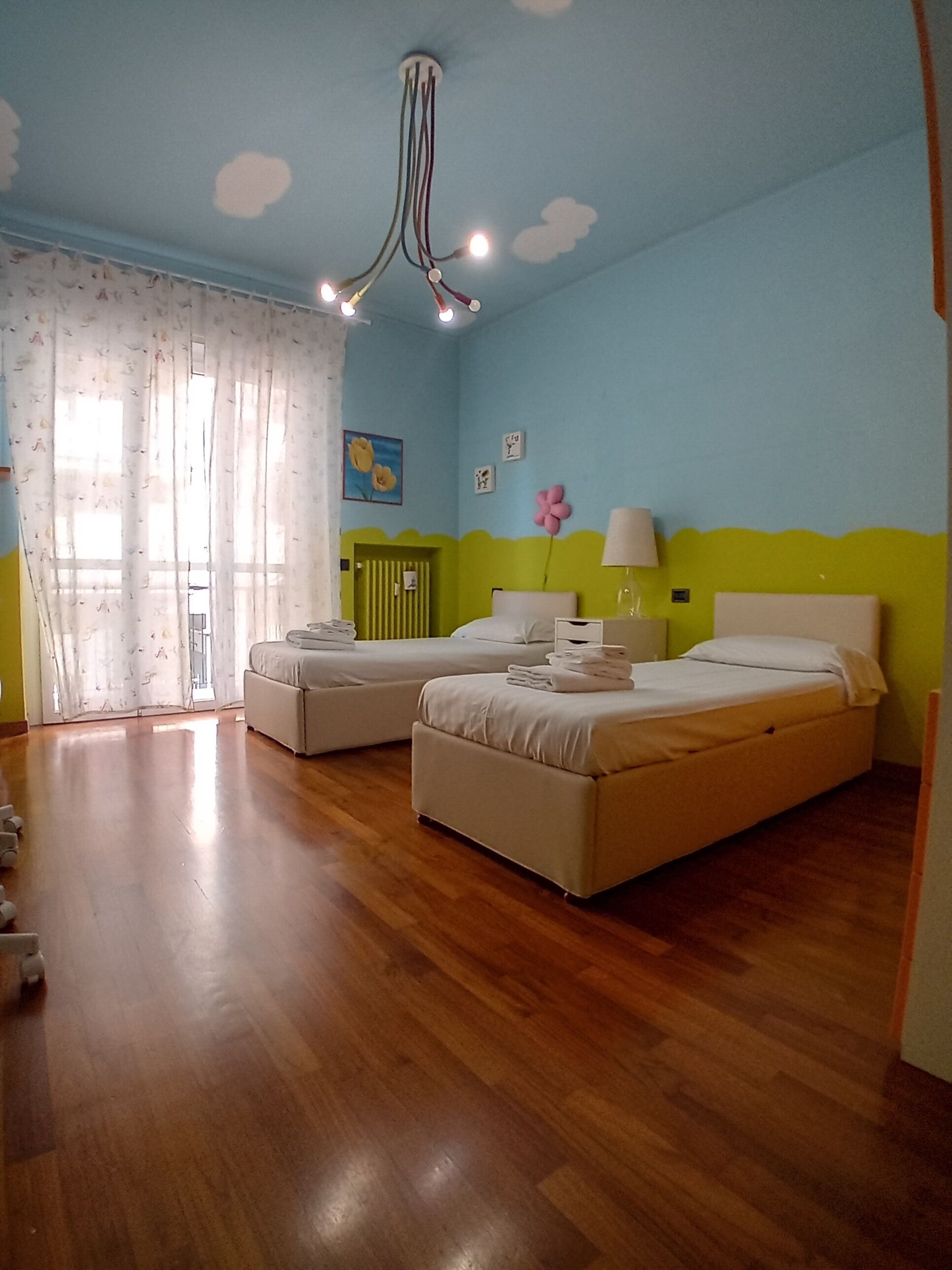 A bedroom with two beds, a green wall, and a ceiling with cloud patterns.