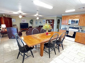 Un grand espace à manger avec une table et des chaises en bois, une cuisine dotée de meubles et d’appareils électroménagers en bois, et un ventilateur de plafond.