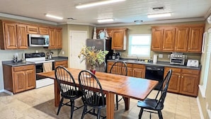 Una cocina con armarios de madera, una mesa de comedor con sillas, un refrigerador, un microondas, una estufa y un lavavajillas.