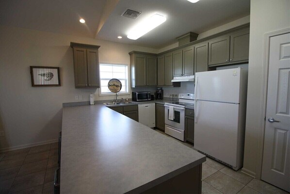 A kitchen with a large island, built-in microwave, oven, and refrigerator. There is a window with blinds and a framed picture on the wall.