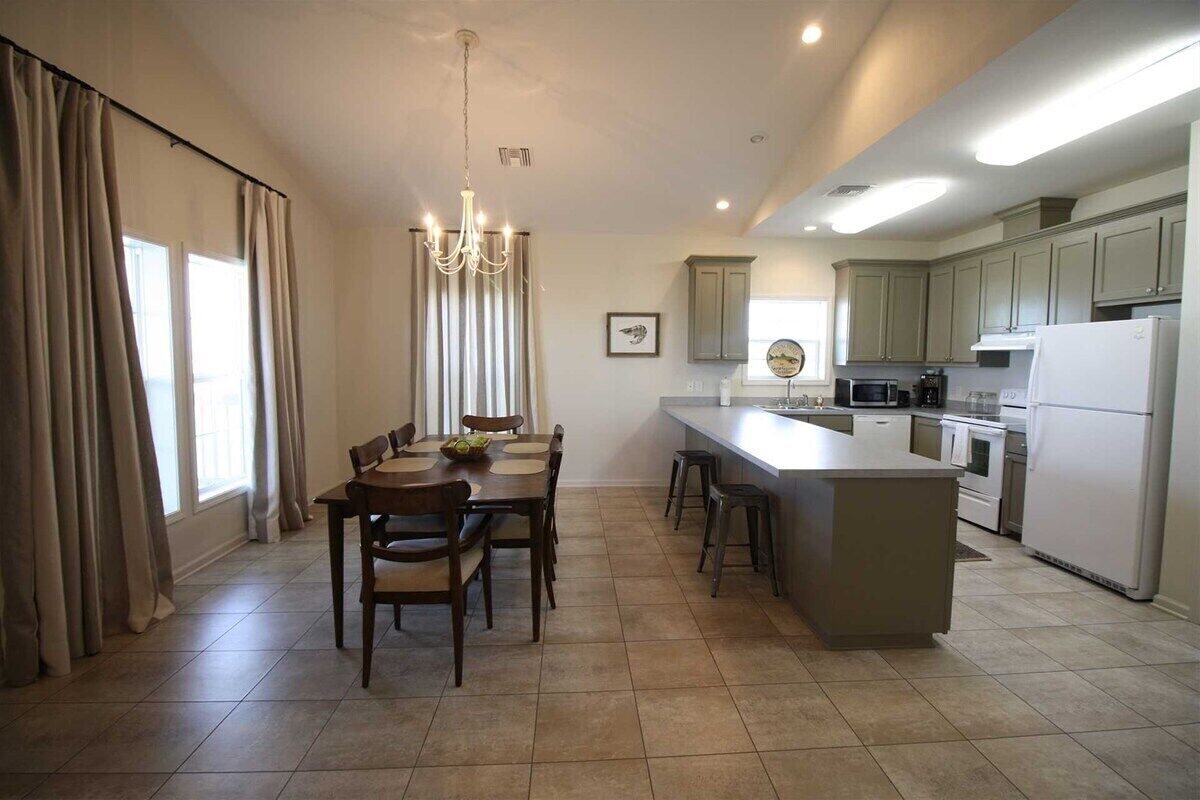 Una cocina moderna con zona de comedor, que cuenta con una isla central, iluminación colgante y vistas al comedor.
