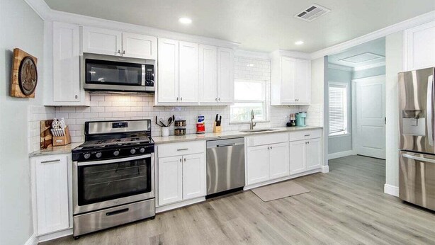 A modern kitchen with white cabinets, stainless steel appliances, and a wooden floor.