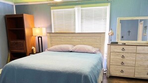 Un dormitorio con una cama, un aparador de madera, una mesita de noche y una ventana con persianas.