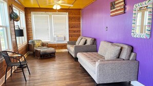 Una habitación acogedora con techo de madera, pared morada y sofá gris.
