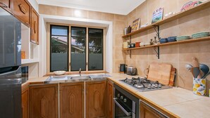 Ett kök med träskåp, en diskho i rostfritt stål, en gasspis och ett fönster med utsikt över ett hus.