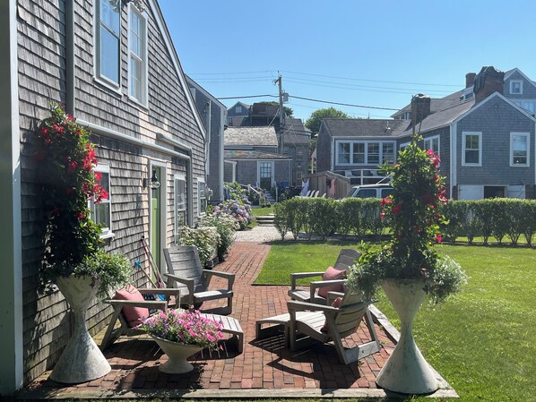 A patio with outdoor furniture and potted plants, a brick pathway, and a residential neighborhood in the background. - Renovated 2024, Blocks From the Inner Harbor/ Downtown - King, Twins, Pull out. (Nantucket)