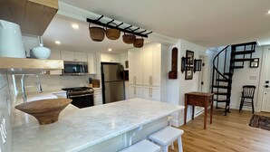 A modern kitchen with white cabinetry, a large marble island, and a wooden bench. - Renovated 2024, Blocks From the Inner Harbor/ Downtown - King, Twins, Pull out. (Nantucket)