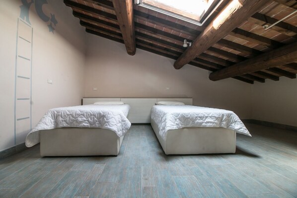 Una habitación con dos camas, un tragaluz, vigas de madera y una escalera.