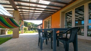 An outdoor patio with a table and chairs, a hammock, and a building with large windows. - Limonaia, one-bedroom terraced house PLUS (Cecina)
