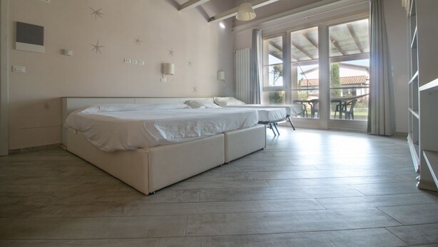 A bedroom with a large bed, a small table, and a view of the outdoors. - Limonaia, one-bedroom terraced house PLUS (Cecina)