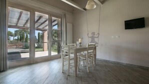 A spacious room with a large sliding glass door leading to an outdoor area, a dining table with chairs, and a flat-screen TV mounted on the wall. - Limonaia, one-bedroom terraced house PLUS (Cecina)