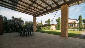 A covered patio with a table and chairs, a hammock, and a view of a residential area with houses and trees. - Limonaia, one-bedroom terraced house PLUS (Cecina)