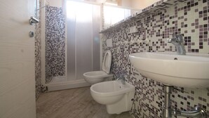 A bathroom with a shower, two bidets, a sink, and mosaic tile walls. - Limonaia, one-bedroom terraced house PLUS (Cecina)
