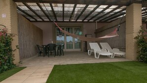 Un patio couvert avec un hamac, des chaises d’extérieur et une table à manger.