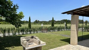 A stone barbecue grill in a grassy outdoor area with a tiled patio and a pergola structure. - Colombaia, one-bedroom terraced house (Cecina)