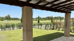 A covered outdoor area with stone pillars, a paved floor, and a view of a grassy field with trees and a sign. - Colombaia, one-bedroom terraced house (Cecina)