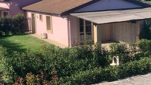 Ein rosafarbenes Gebäude mit Ziegeldach, einer überdachten Veranda und einem kleinen Garten.