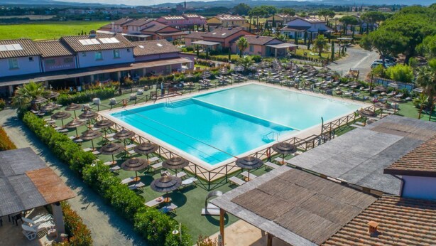 Una piscina grande rodeada de tumbonas y sombrillas, con villas al fondo.