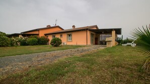 A house with a paved driveway, a covered porch, and a small garden area. - Limonaia , one-bedroom terraced house (Cecina)