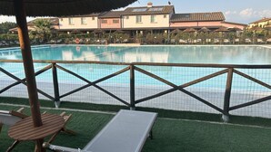 A pool area with a wooden fence, lounge chairs, and a building with a sign that reads "LE CANTINE" in the background.