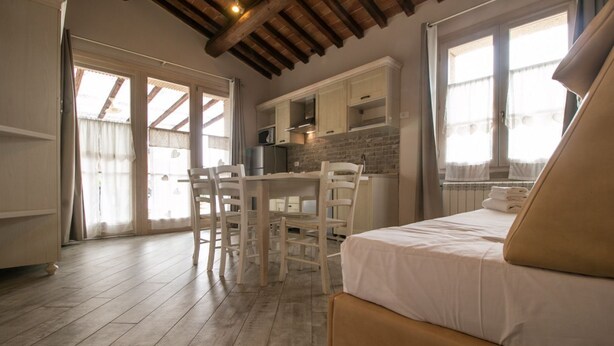 Quarto com cama, mesa de jantar com cadeiras, área de cozinha e uma janela grande.