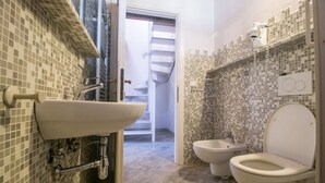 Une salle de bain équipée d’un lavabo, de toilettes, d’un bidet et d’un mur recouvert de carreaux formant une mosaïque.