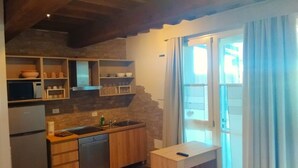 Eine kompakte Küche mit Holzausstattung, einer eingebauten Mikrowelle und einem Spülbecken. Ein Fenster mit Vorhängen bietet einen Blick nach draußen.