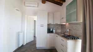 A modern kitchen with light wooden cabinets, a gas stove, and a microwave. - Fienile building, two-bedroom terraced house (Cecina)