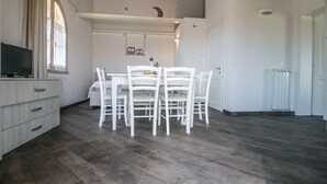 A dining area with a white table and chairs, a television on a cabinet, and a window with curtains. - Fienile building, two-bedroom terraced house (Cecina)