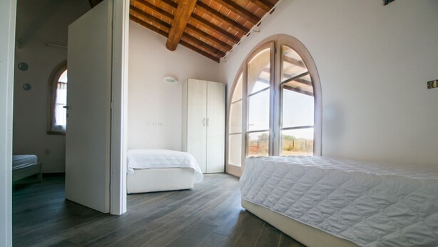 A bedroom with a large arched window, a wooden ceiling, and a white wardrobe. - Fienile building, two-bedroom terraced house (Cecina)