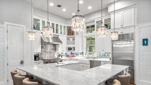 A modern kitchen with a large island, bar stools, stainless steel appliances, and pendant lighting. - Lake District Luxury: 6-Bedroom Retreat with WaterColor Beach Club Access, Bikes, and Electric Cart! (Santa Rosa Beach)