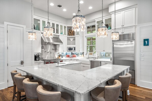A modern kitchen with a large island, bar stools, stainless steel appliances, and pendant lighting.