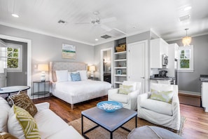 A modern hotel room with a large bed, a sitting area with a sofa and armchairs, a small table, and a kitchenette. - Lake District Luxury: 6-Bedroom Retreat with WaterColor Beach Club Access, Bikes, and Electric Cart! (Santa Rosa Beach)