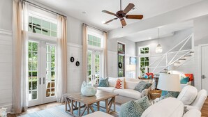 A spacious living room with a white sofa, a wooden coffee table, and a ceiling fan. - Lake District Luxury: 6-Bedroom Retreat with WaterColor Beach Club Access, Bikes, and Electric Cart! (Santa Rosa Beach)