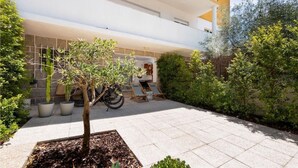 A courtyard with a tree, potted plants, and outdoor seating. - The 98 Place (Carcavelos)