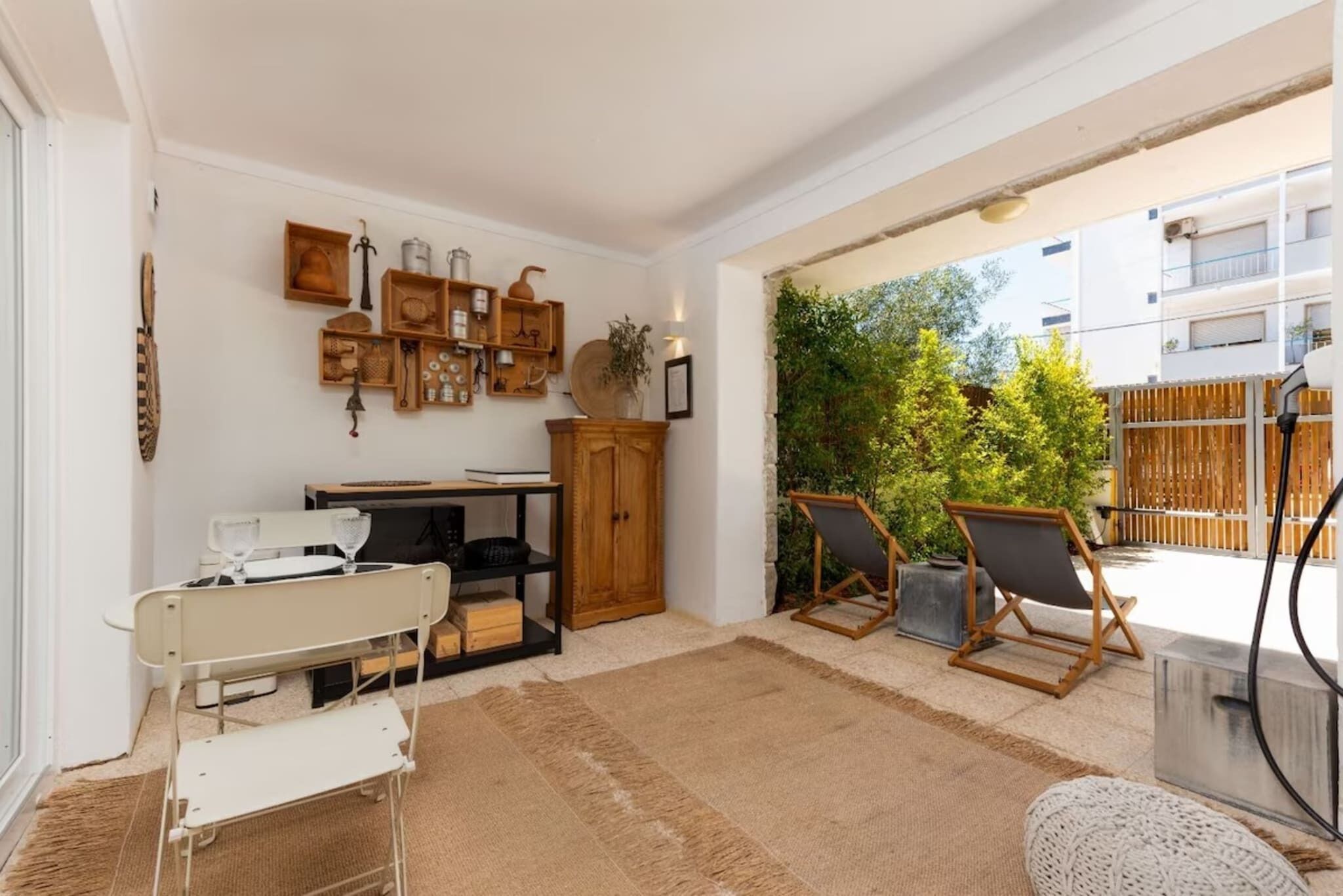 A cozy living room with a white sofa, a wooden cabinet, and a small table. There are two chairs and a rug on the floor.