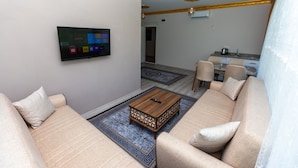 Una sala de estar moderna con televisor de pantalla plana, sofá color beige, mesa de centro y zona de comedor al fondo.