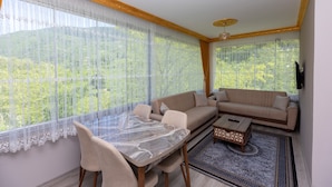 Un salón con sofá, una mesa y una mesita de centro. Hay cortinas en las ventanas y una alfombra en el suelo.