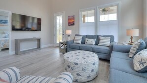 Ein Wohnzimmer mit blauem Sofa, rundem Hocker und Flachbildfernseher.