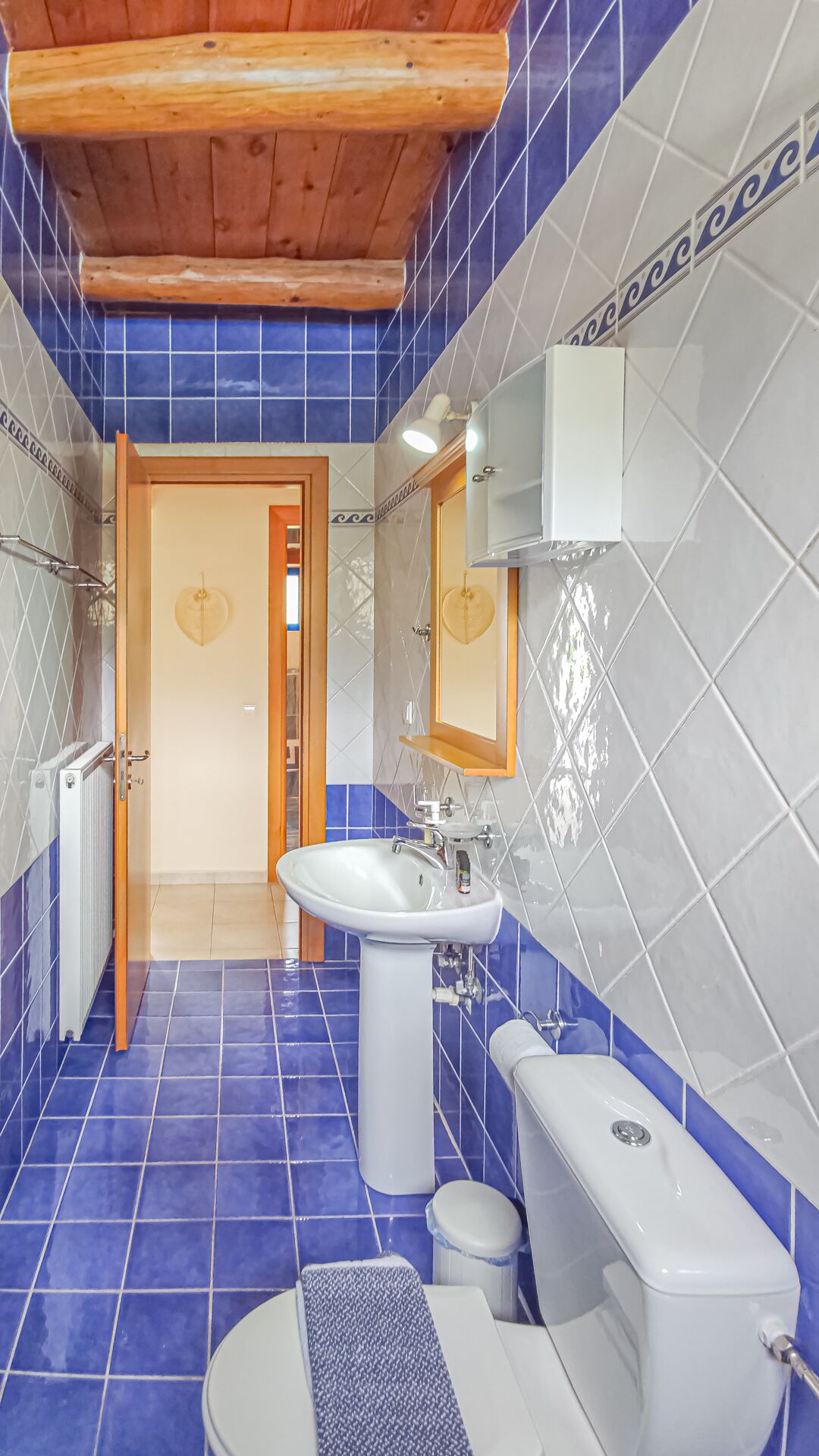 A bathroom with blue tiles, a white sink, a toilet, and a shower area.