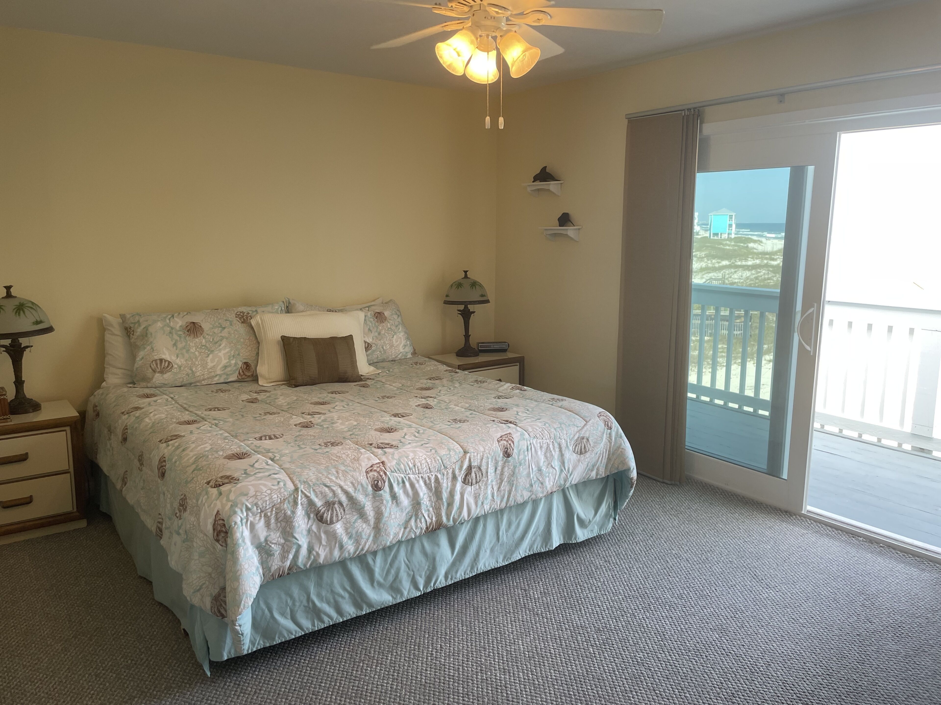 A bedroom with a bed, two bedside tables, a ceiling fan, and a view of the outdoors through a sliding glass door.