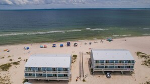 Un hotel frente a la playa con una estructura de dos pisos, una playa de arena con sombrillas y el océano al fondo.