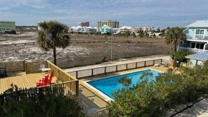 Un área de piscina con un muelle de madera, una silla roja y vistas a la playa y edificios al fondo.