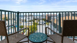 A balcony with wicker chairs and a mosaic table, overlooking a residential area with buildings and a clear sky. - Avalon 507-Oceanside 140th St, Free WiFi, Pool, Elev, W/D, AC (Ocean City)