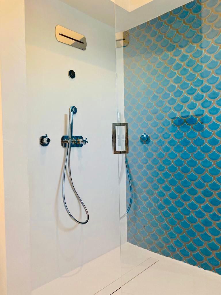 A shower with a glass enclosure, a control panel, and a blue patterned wall.