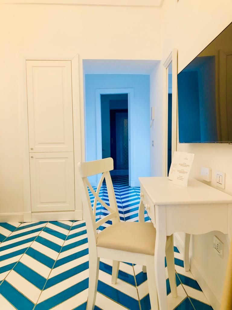 Une pièce avec une porte blanche, un bureau blanc, une chaise et un sol à rayures bleues et blanches.