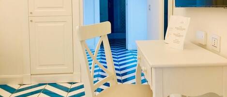 Une pièce avec une porte blanche, un bureau blanc, une chaise et un sol à rayures bleues et blanches.