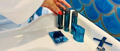 A hand placing a blue bottle into a sink with a white countertop and a blue tiled wall in the background.