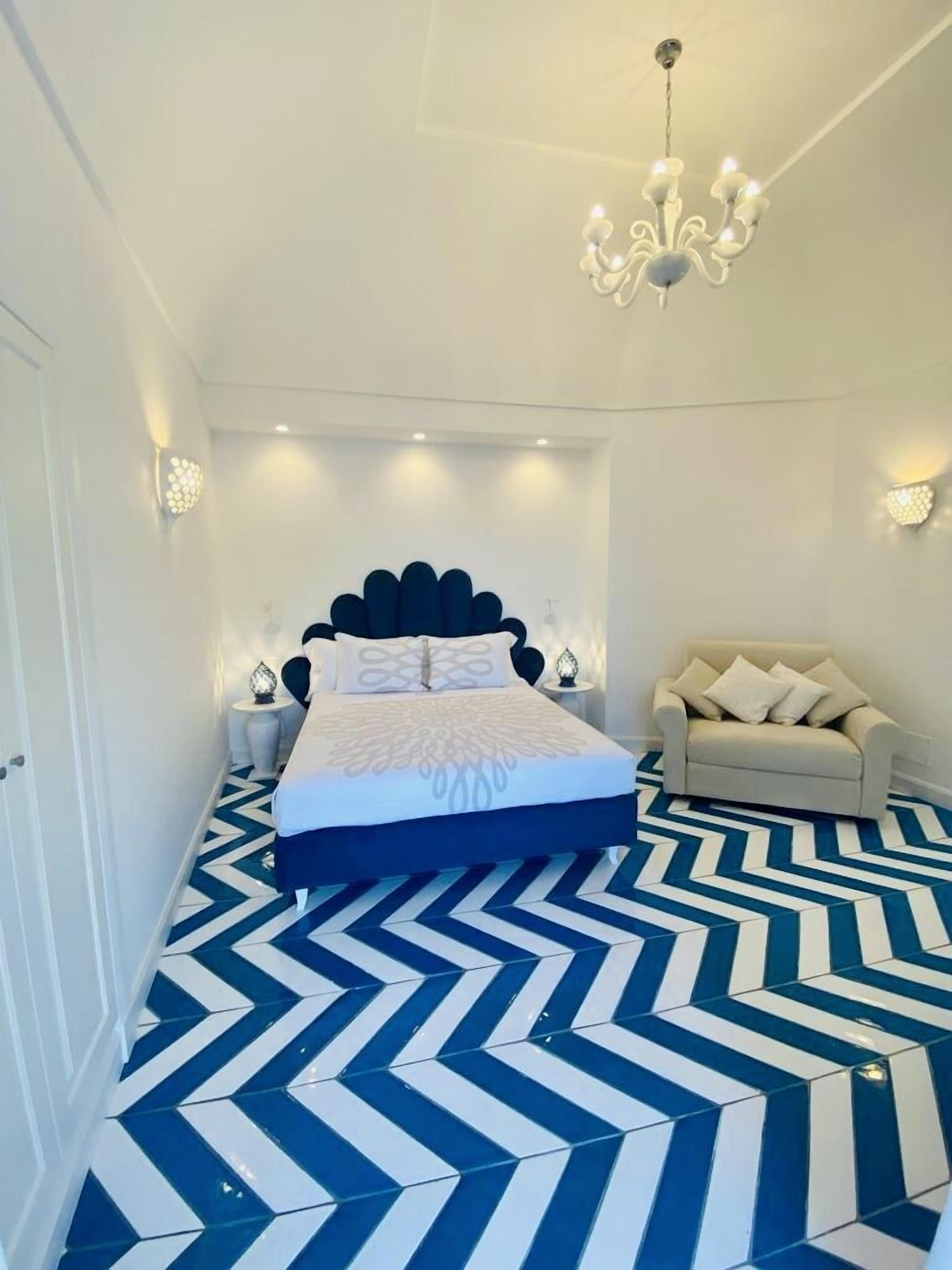 A bedroom with a large bed, a chandelier, a sofa, and a patterned floor.